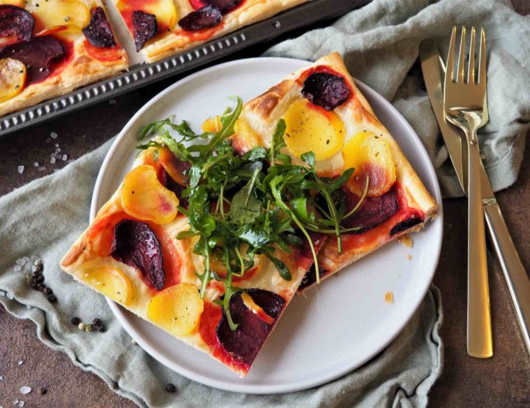 Vegane Blätterteigpizza mit Gelber und Roter Bete und Rucola-Garnitur angerichtet auf Teller